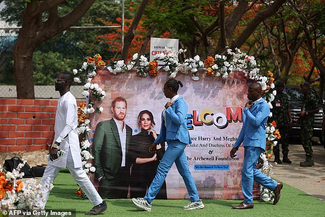 People walk past a sign welcoming Harry and Meghan to Abuja, Nigeria, this morning.