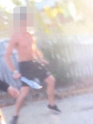 A shirtless man is seen holding a large silver machete during an alleged stabbing at his home.