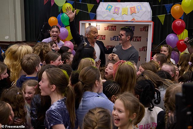 The children are completely surprised and proceed to surround Simon and Bruno, high-fiving each other.