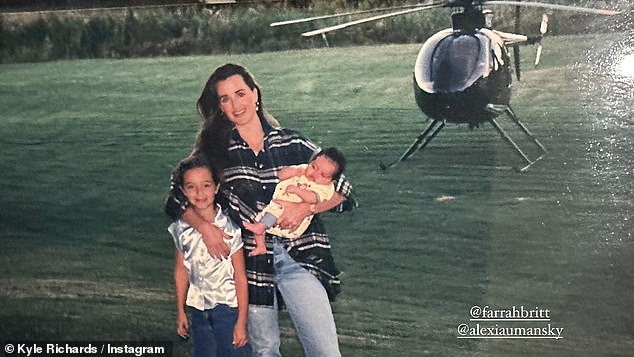 In another photo, the reality TV star wore an oversized blue plaid shirt and jeans while holding baby Alexis.  She has an arm around her daughter Farrah as she stands on the shore of a lake with a helicopter hovering in the background.