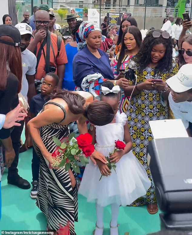 In a touching moment, Meghan Markle, who appeared in a £2,275 embroidered Joanna Ortiz Tropicana Nights dress, printed with black and white palm leaves, chats with a little girl.