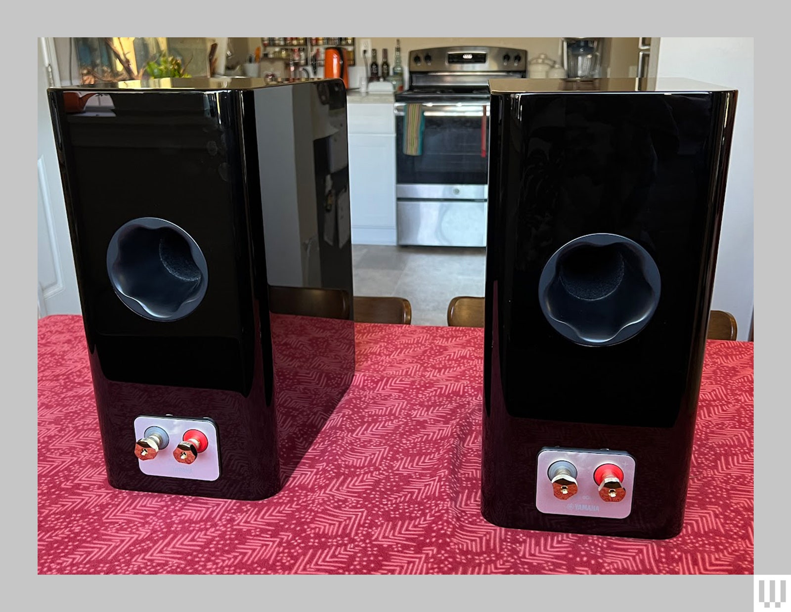 Rear view of two glossy black speakers showing a circular indentation and 2 posts on each