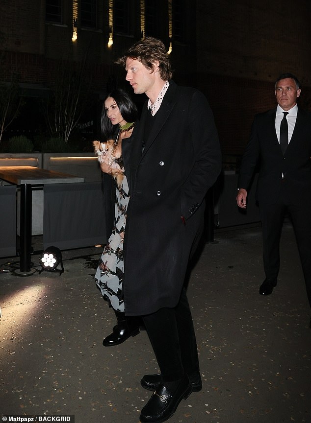 Nikolai looked ahead as Demi spoke to him while holding a dog.