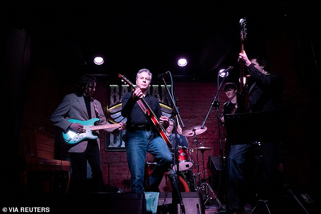 Wearing sporty jeans, black sneakers and a black button-down shirt, Blinken strapped to a red guitar.