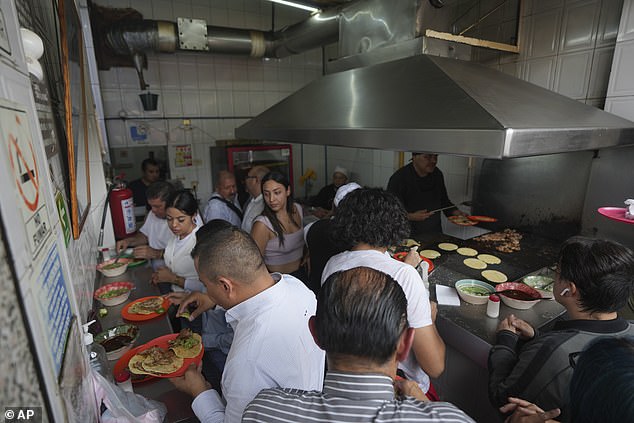 An aerial view of the small taco stand. Customers line the side wall as they put salsa on their tacos, while the Michelin-starred chef continues to serve food.