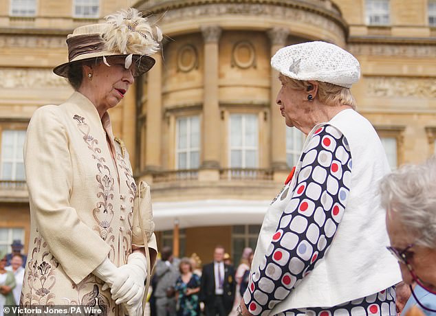 Princess Anne chats with a woman dressed in a white printed outfit at Buckingham Palace today.