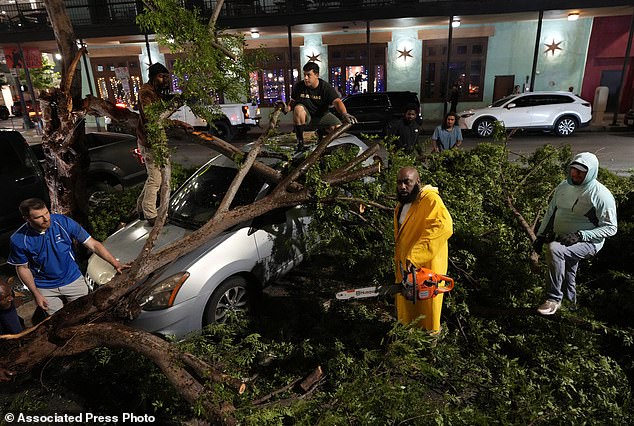 Rapper Trae tha Truth, dressed in yellow, cuts branches from fallen trees on top of a car after a severe storm hit the city center on Thursday.