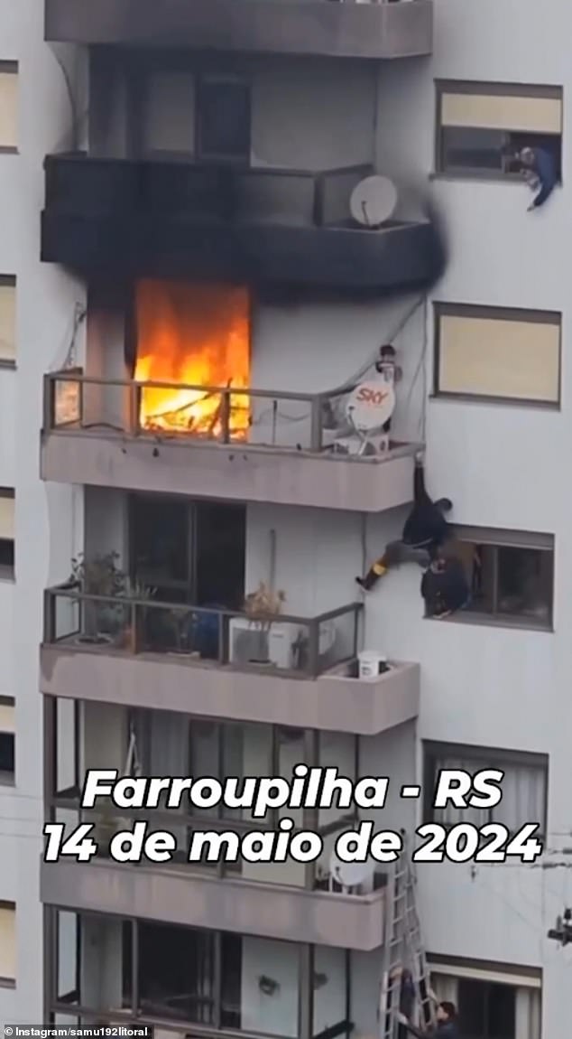 A firefighter climbs from the balcony below, balanced precariously on a window sill as he tries to reach the trapped child.