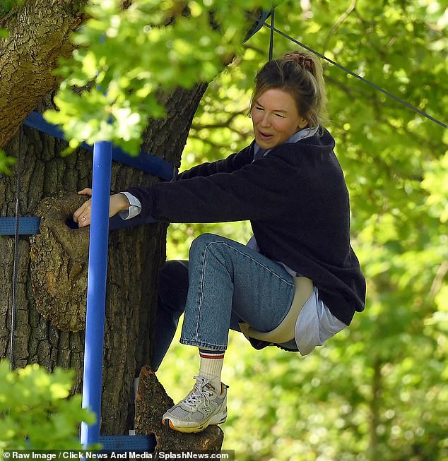 A smiling Mrs. Zellweger hugs the tree, dressed in blue jeans, a shirt and a sweater for the scene.