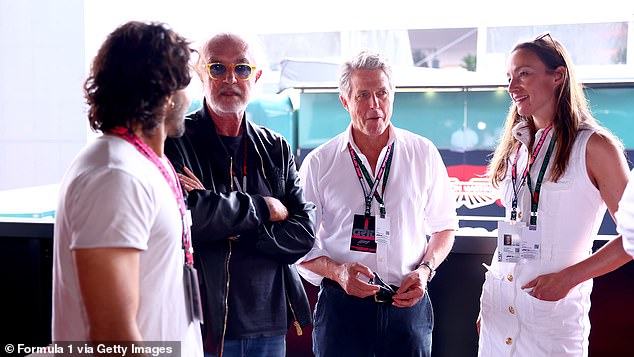 Hugh appeared deep in thought as he chatted to others at the Grand Prix while his wife smiled as she spoke.