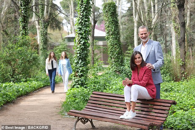 In a more artistic pose, Letizia sits on a bench with her husband behind, while the couple's daughters can be seen in the distance.