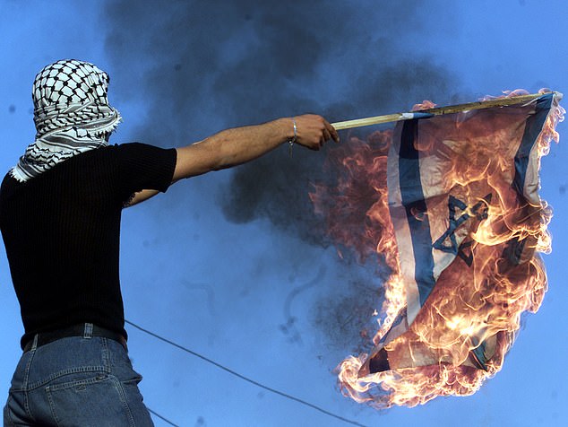 A man wearing a keffiyeh burns an Israeli flag