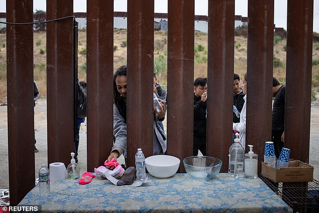 Asylum seekers drink water and socks donated by a charity as they wait to surrender to US immigration officials at the California-Mexico border.