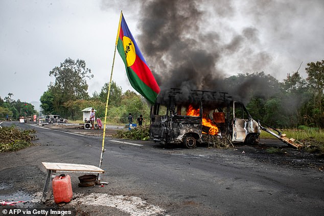 A Kanak flag flying next to a burning vehicle at a roadblock in La Tamoa, in the commune of Paita in New Caledonia.