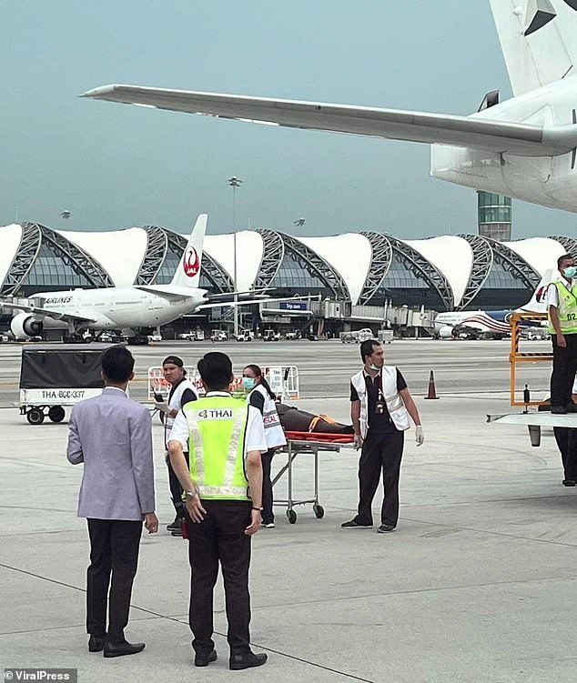 A person is seen being taken off the plane on a stretcher today in Bangkok.