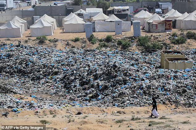 A woman retrieves items from a waste dump that sprawls across a tent displacement camp west of Nuseirat in the Gaza Strip on May 21, 2024.