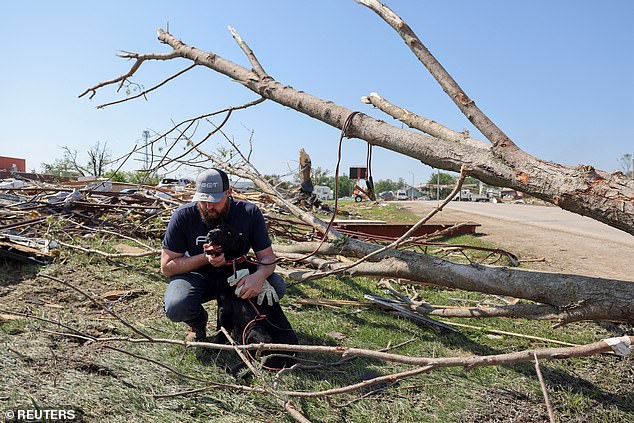 Phillip Ergish of Greenfield, Iowa, holds his dog Kobe as he surveys the remains of his home.