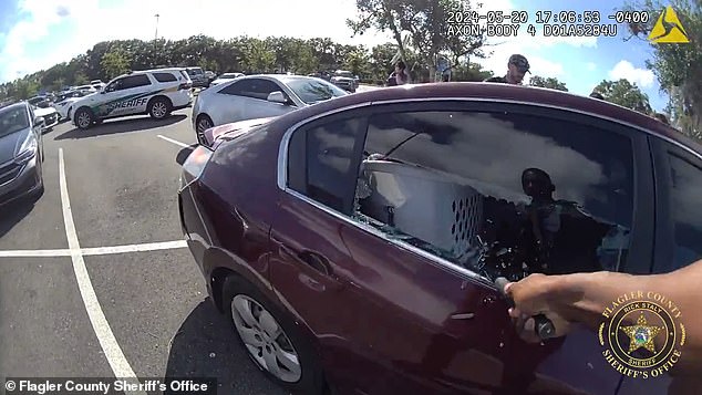 The officer is seen breaking the window with a tool while the other officer talks to the adult on the other side of the vehicle.