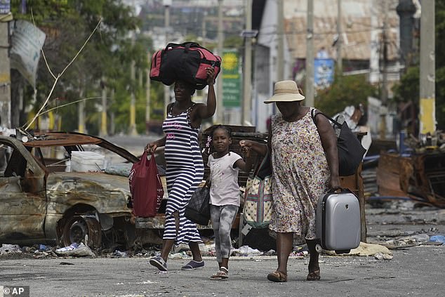 A girl is led by the hand next to a burned-out car blocking the street as residents evacuate the Delmas 22 neighborhood to escape gang violence in Port-au-Prince, Haiti, on May 2.