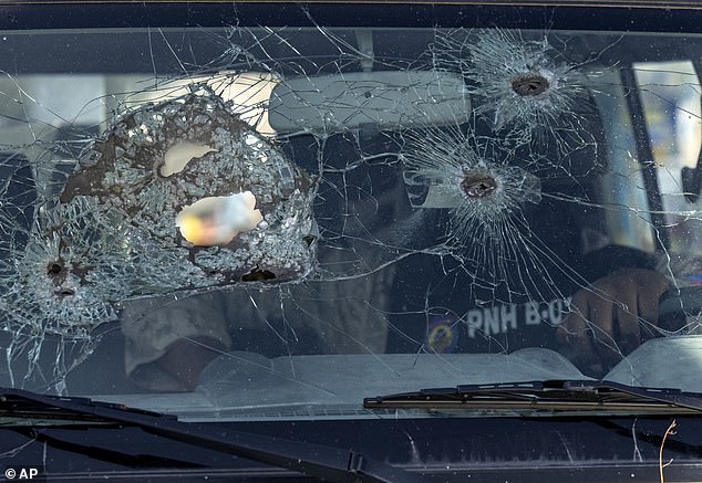 A police officer sits inside his vehicle with the windshield damaged by bullet holes, in Port-au-Prince, Haiti, Saturday, May 11, 2024.