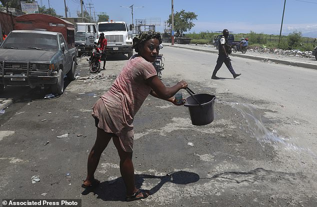 A woman covers the side of the road with water to prevent dirt from rising, as police patrol near Port-au-Prince airport.