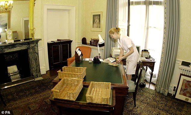 A cleaner hard at work, before staff arrive at one of the many desks in an office at Buckingham Palace, 2000.