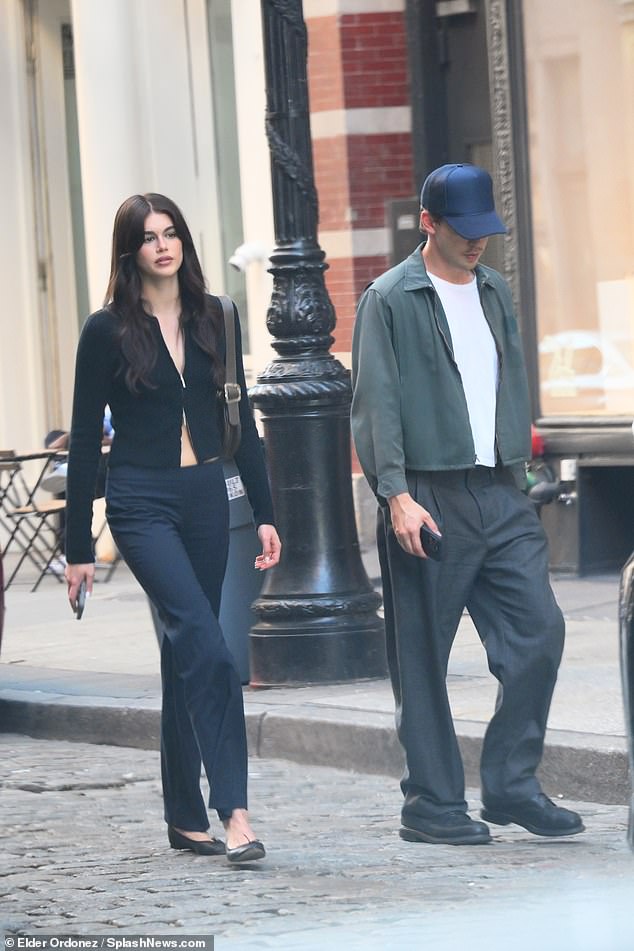 Kaia looked stunning in a long-sleeved black top with a button-down in the middle, revealing stripes of chest and abs.  The Palm Royale actress, 22, paired the chic top with low-rise dark jeans and black ballet flats.