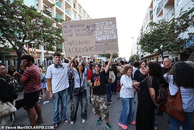 Protesters in Ibiza hold signs, including one that says 