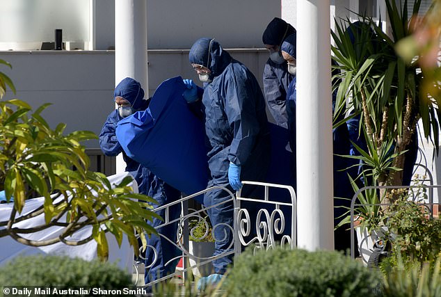 In the photo, police remove a body from the house where the double suicide occurred.