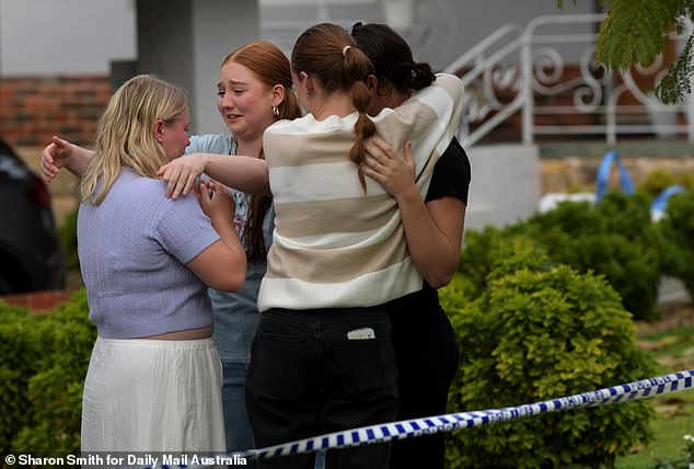 Pictured: Mourners comfort each other after leaving floral tributes outside the crime scene.