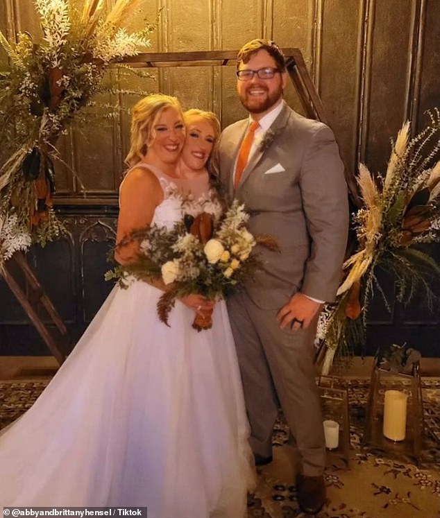 Abby and Brittany pose with Josh holding a bouquet of flowers in front of the display and candles.