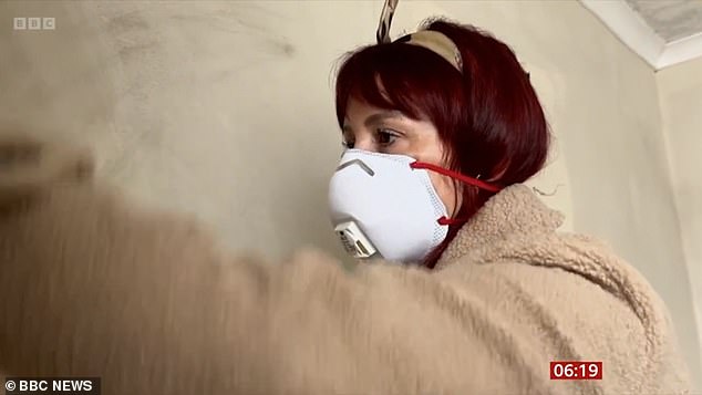 Godrich wears a mask as he cleans mold from the walls covering his house.