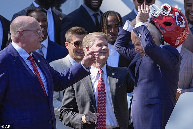 Kansas City Chiefs coach Andy Reid (left) and CEO Clark Hunt (center) help President Joe Biden remove the helmet that was brought to the White House as a gift from the team.