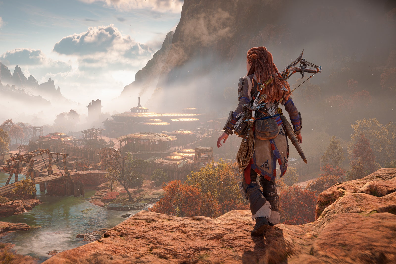 Screenshot from Horizon Forbidden West showing a character walking along a mountain ridge in front of a small town.