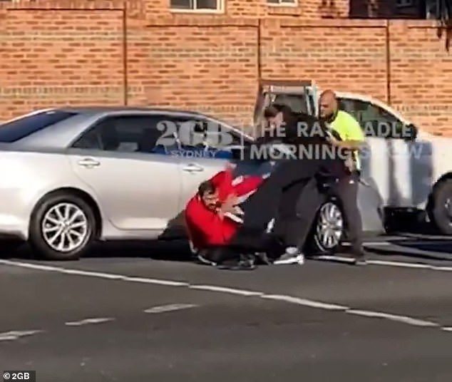 A trader is shown trying to break up a wild brawl on a Sydney road on Wednesday morning.