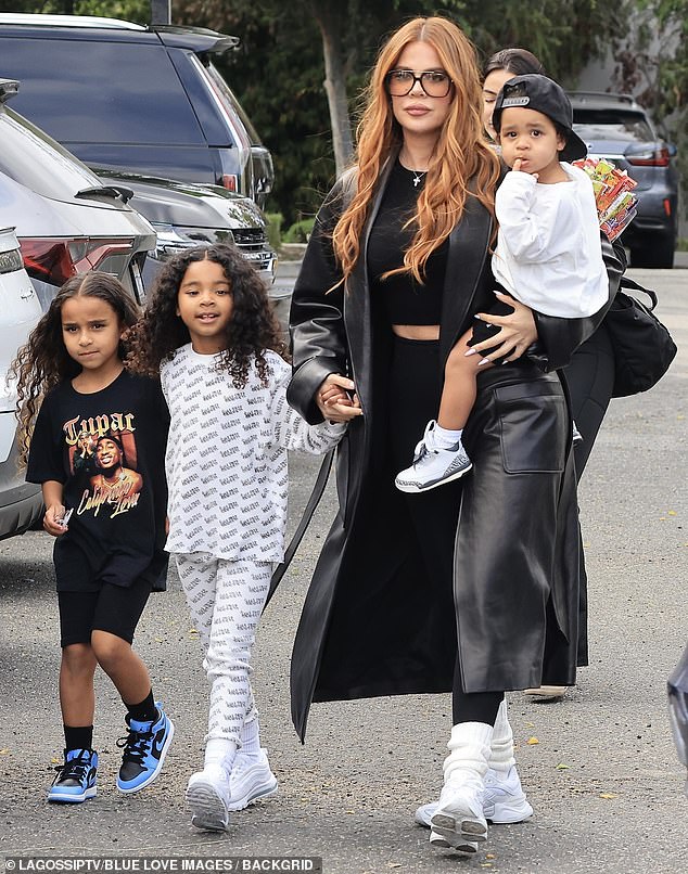 Khloé's red hair matched the lenses of her retro plastic aviator glasses, completing the look with a silver cross necklace and white sneakers with matching tube socks.