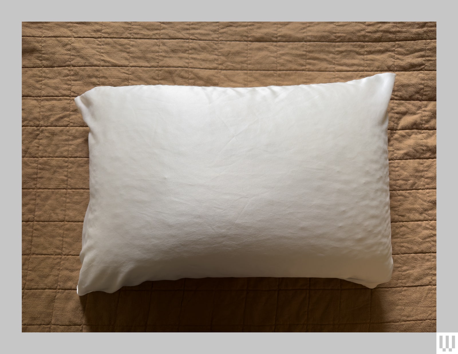 Overhead view of a pillow with a white silk cover on top of a beige duvet