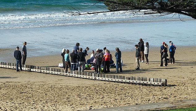 A man died after being pulled from the waters off Cozy Corner Beach in Torquay, along Victoria's surf coast, at 9.45am on Saturday (pictured: paramedics and bystanders at the scene).