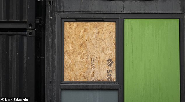 A broken window is boarded up on one of the shipping container's floors.