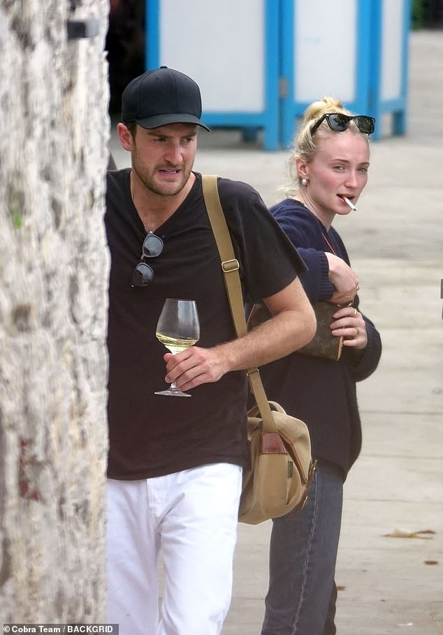 Sophie put her sunglasses on her head while holding the cigarette between her teeth.