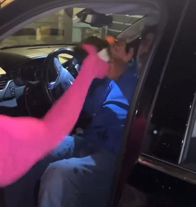 The video shows a woman in a pink sweater pouring liquid on the driver.