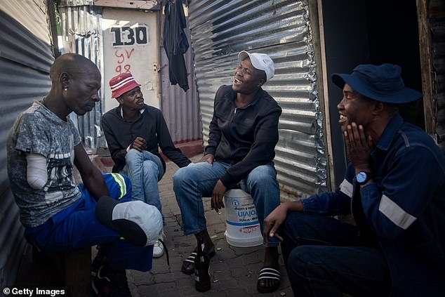 Men joke as they share a beer outside their homes in an informal settlement in Alexandra township on May 31, 2024 in Johannesburg.