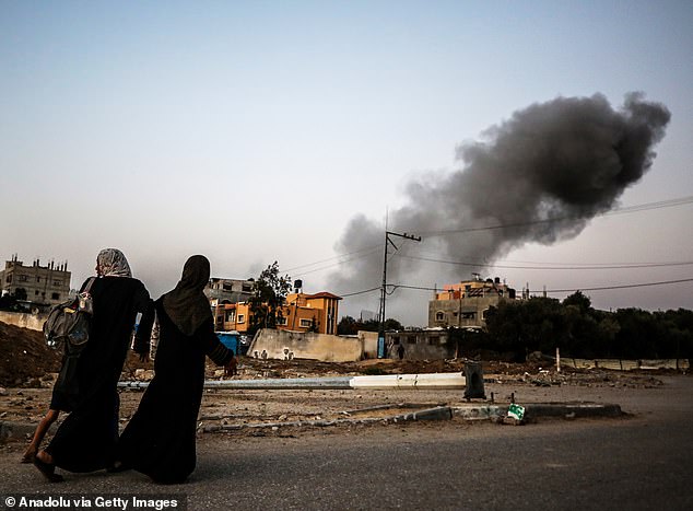 Two Palestinian women walk past the ruins of a building in Al Bureij.