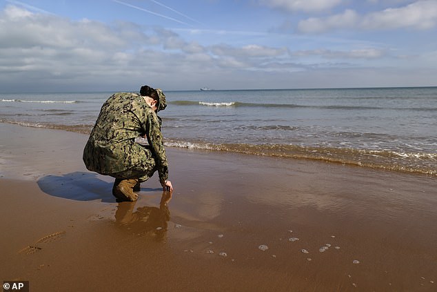 An American soldier touches the sand on Omaha Beach, where more than 4,400 Allied soldiers died 80 years ago.