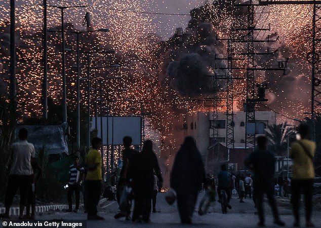 Palestinians on a road as black smoke and flames rise over a building following Israeli attacks in Deir al-Balah, Gaza, on June 6.