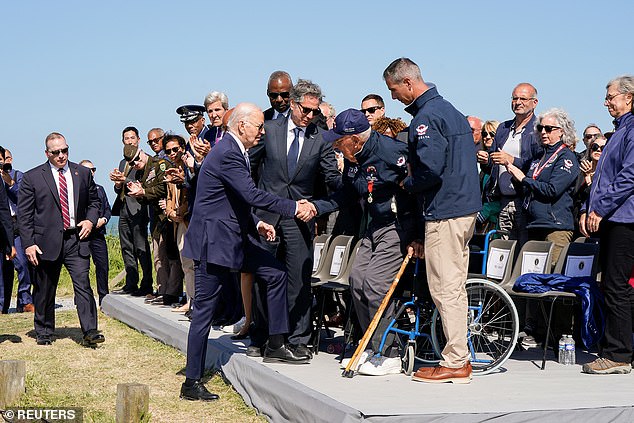 Biden shakes hands with World War II veteran John Wardell, while US Secretary of State Antony Blinken stands next to them.