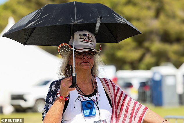 A woman protects herself from the sun with an umbrella while waiting to enter the rally