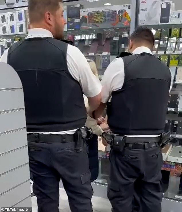 Separate images then show the woman being handcuffed by three police officers inside the store.