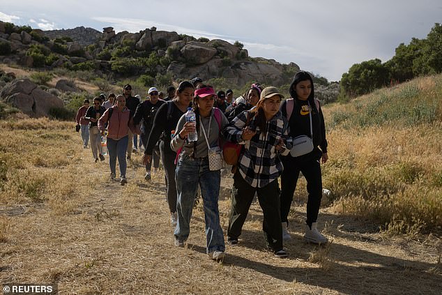 SEI*207607621 Migrants from South and Central America hold hands as they walk toward a gap in the border wall before crossing onto Boulevard, California