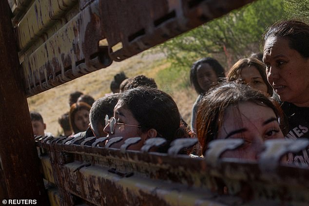 Migrants from South and Central America look toward the United States through a gap in the border wall before crossing into Boulevard, California, as they line up to enter the United States from Tecate, Mexico.